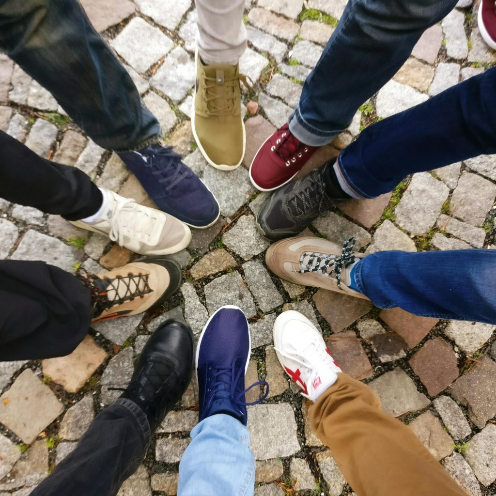 Pourquoi et comment développer un réseau professionnel efficace ? Circle of sneakers on cobblestone pavement representing diversity and urban fashion.