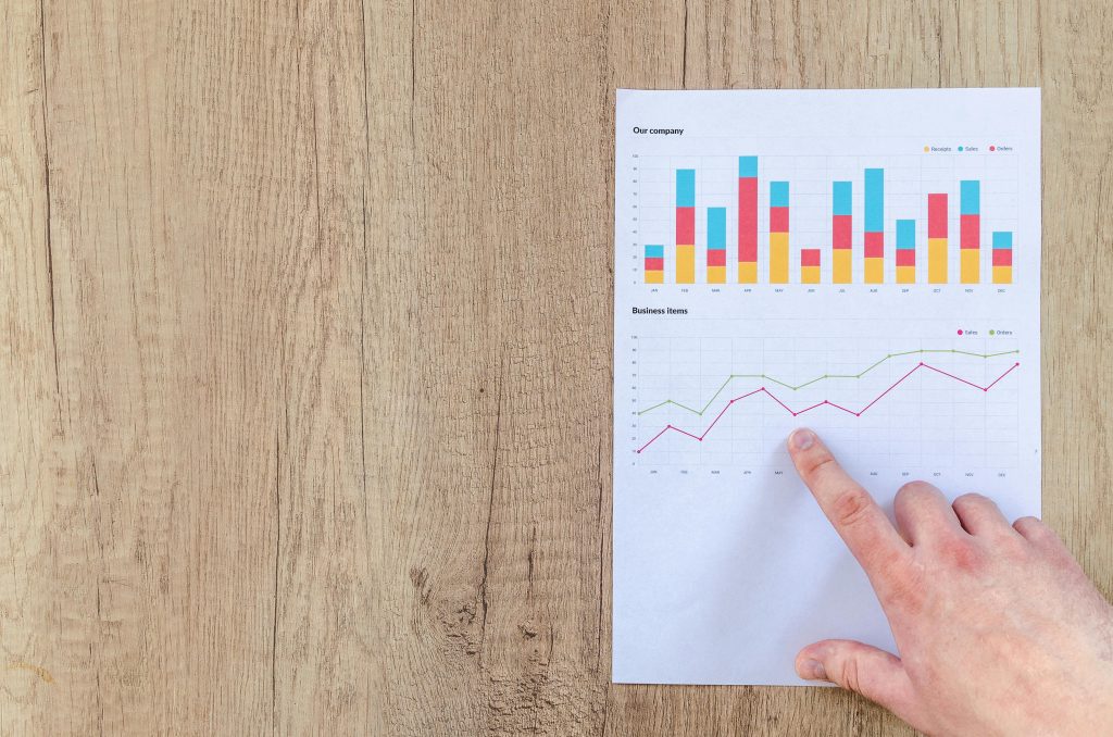 Comment transformer un refus d’embauche en opportunité ? Hand analyzing business graphs on a wooden desk, focusing on data results and growth analysis.