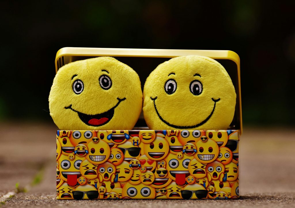 Le storytelling : comment l’utiliser pour vendre plus ? Two yellow smiley plush toys in an emoji-themed box, expressing fun and happiness.