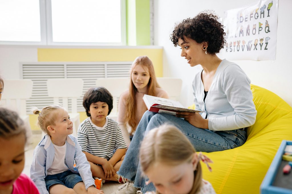 Le storytelling : comment l’utiliser pour vendre plus ? Teacher reading to preschool kids in a colorful classroom setting.