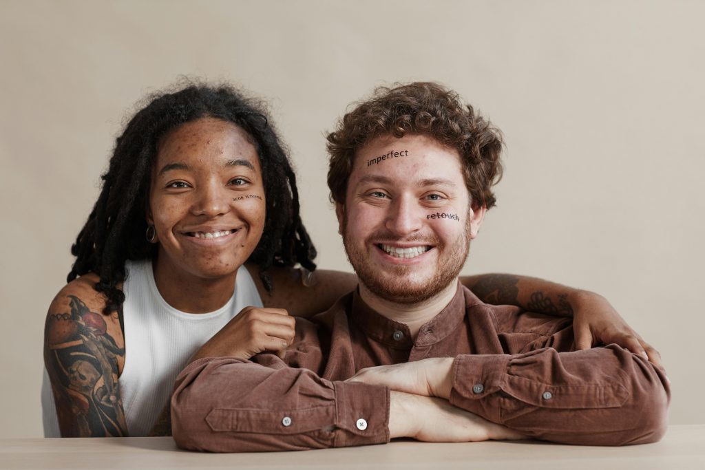 Two diverse adults smiling, promoting self-acceptance with words on their faces.