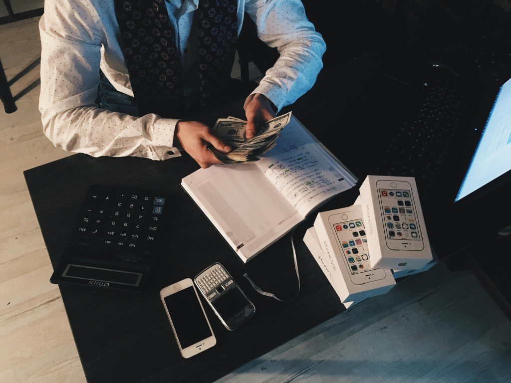 10 astuces simples pour économiser de l’argent chaque mois (débutant / intermédiaire) Businessman organizing finances with tech devices and cash on desk.