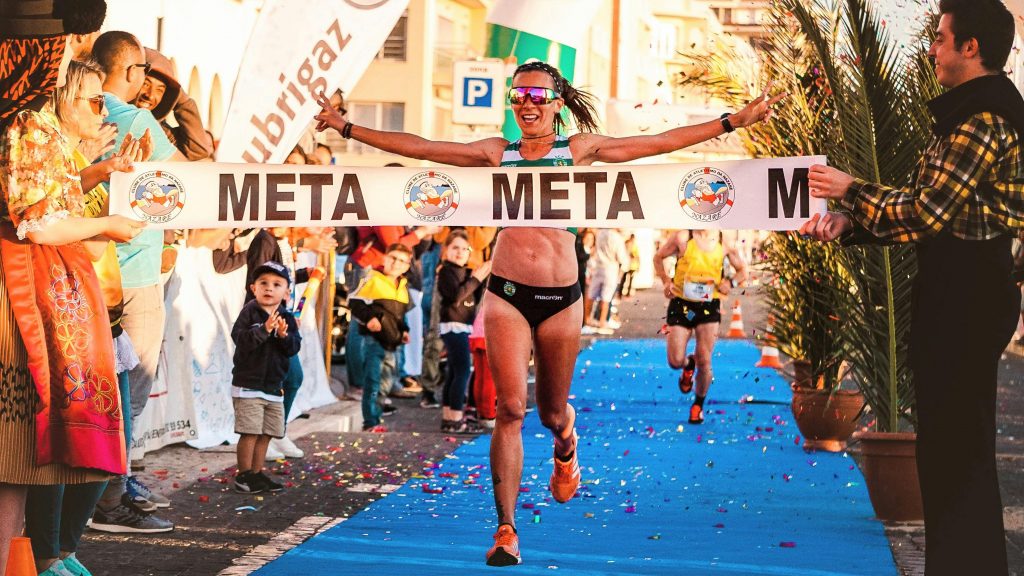 Joyful female runner crosses the finish line at a marathon, celebrating victory.