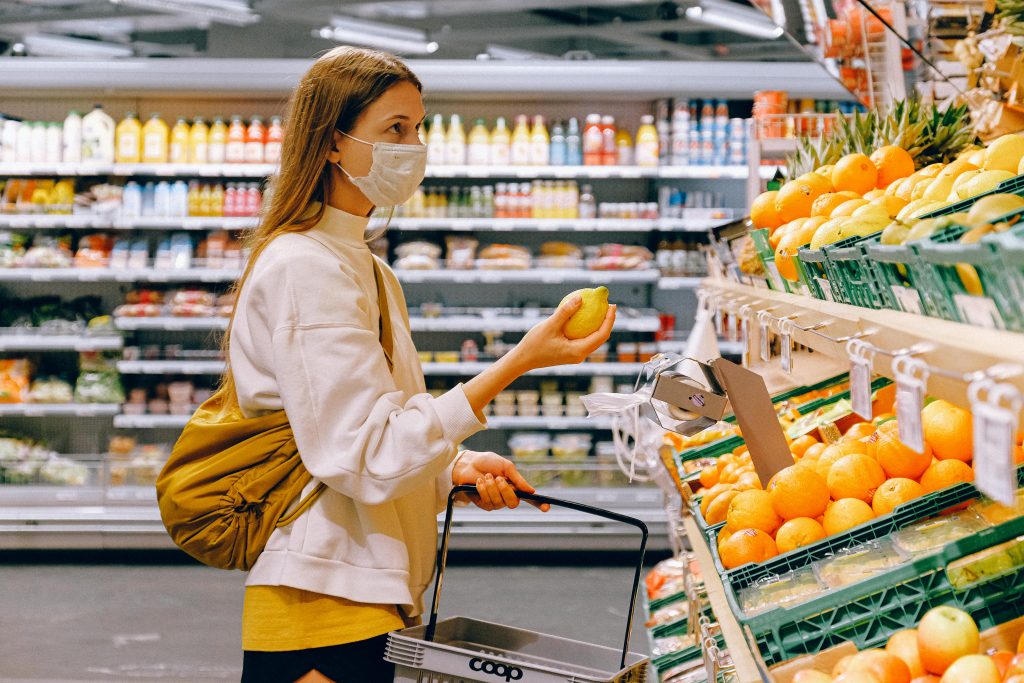 10 astuces simples pour économiser de l’argent chaque mois (débutant / intermédiaire) A woman wearing a face mask shops for fruits in a supermarket during a pandemic.