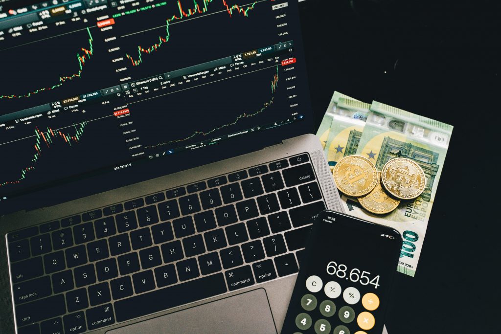 Comment fixer des objectifs financiers réalistes et motivants A laptop displaying stock charts with Bitcoin, Euros, and a cellphone calculator, showcasing financial analysis.