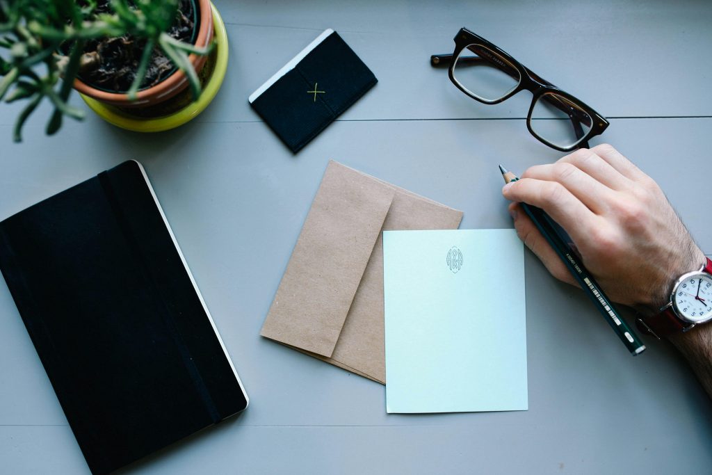 Qu’est-ce que le cash stuffing ou la méthode des enveloppes ? Overhead view of a desk with writing tools, glasses, envelope, and notebooks, showcasing office work essentials.