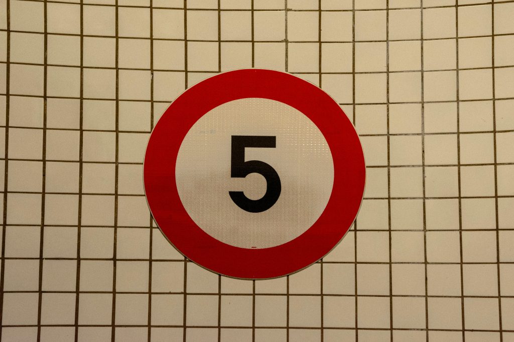 Close-up of a speed limit sign with the number 5 against a tiled wall background.