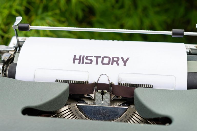 Close-up of a vintage typewriter with a paper labeled 'History' in an outdoor setting.