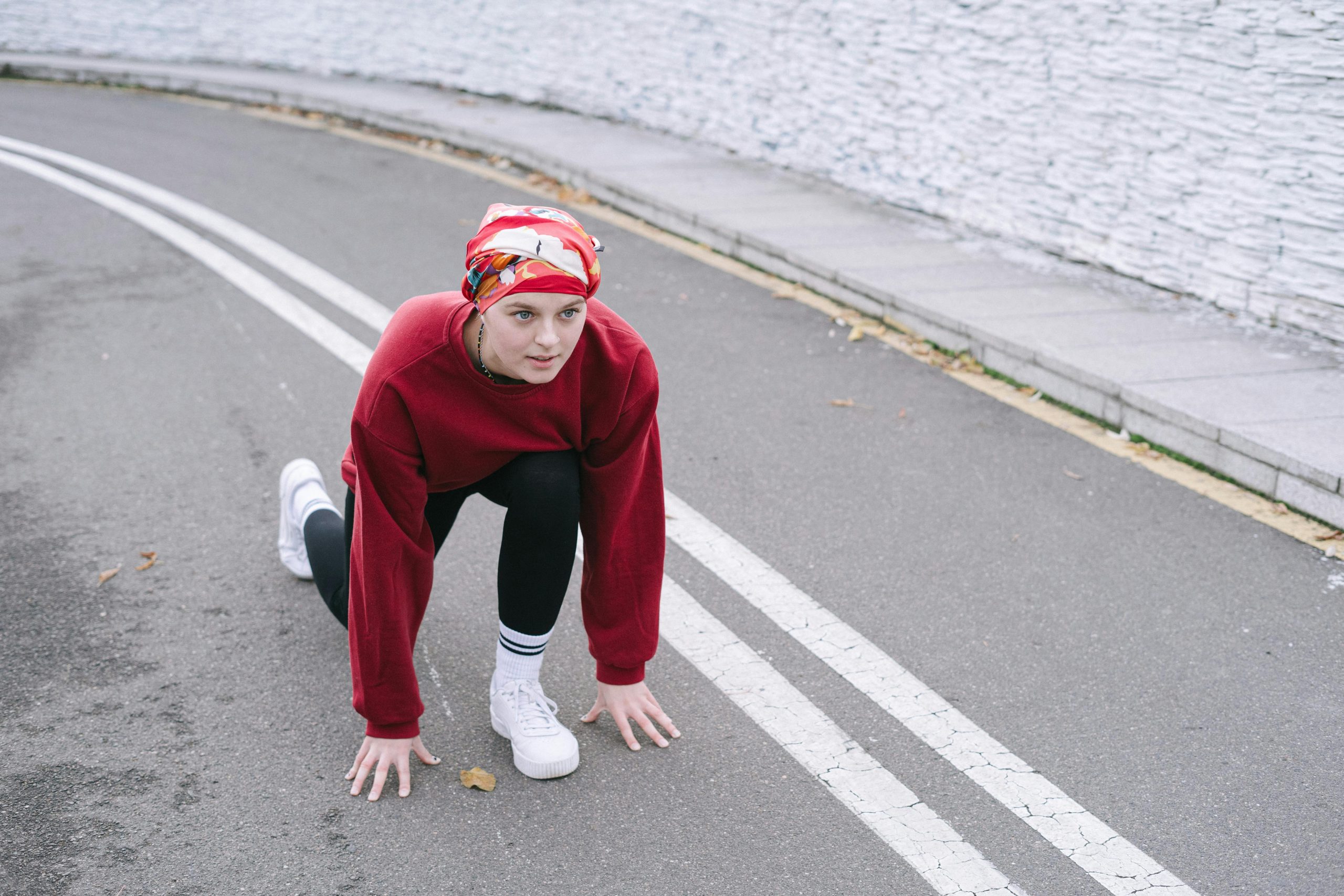 Woman in athletic wear getting ready for a sprint start on a city road.