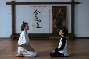 mes articles A karate trainer and child meditating on a wooden floor in a dojo setting.