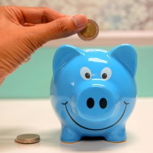 Hand inserting a coin into a blue piggy bank for savings and money management.