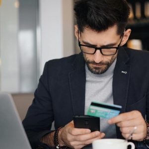 Businessman making online payment with smartphone and credit card in a modern café.