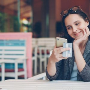 Smiling woman using smartphone and credit card at cafe for online shopping.