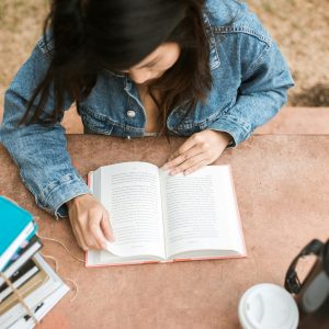 Overhead view of a woman reading a book outdoors on a sunny day, wearing a denim jacket.