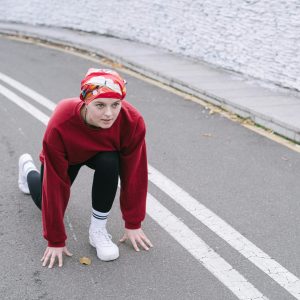 Woman in athletic wear getting ready for a sprint start on a city road.