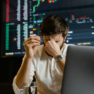 A stressed man looks at stock market data on his computer screen in an office setting.