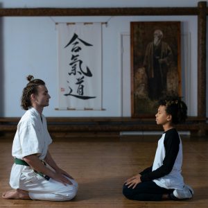 A karate trainer and child meditating on a wooden floor in a dojo setting.
