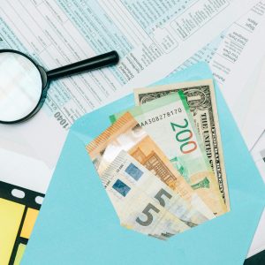 Close-up of tax documents and mixed currency in a blue envelope with a magnifying glass, perfect for financial analysis concepts.